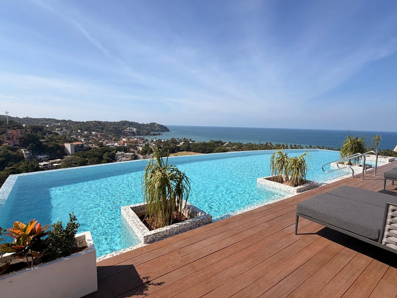 Alberca turquesa con jardineras y deck frente al mar