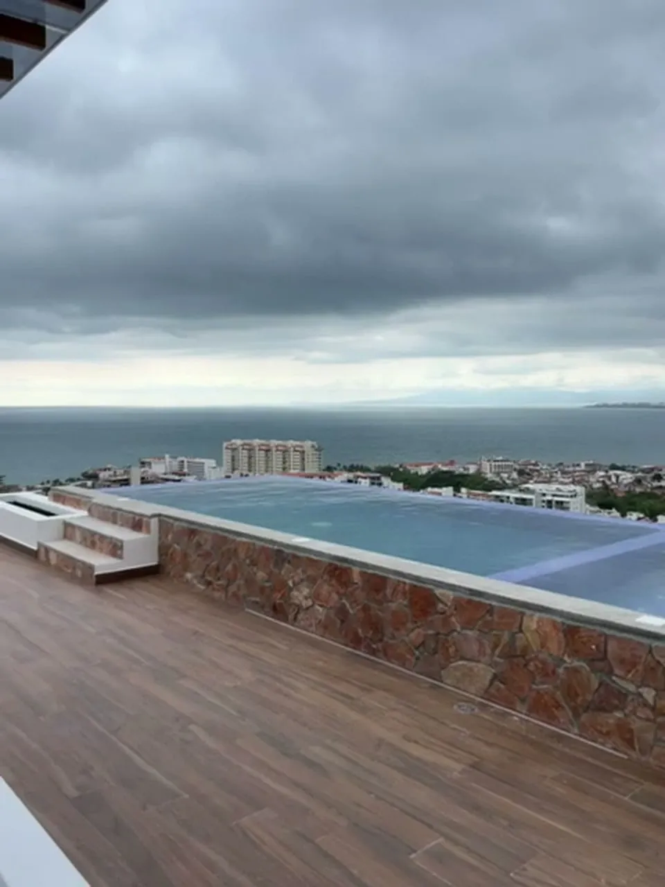 Alberca revestida de piedra con deck de madera y vista al mar